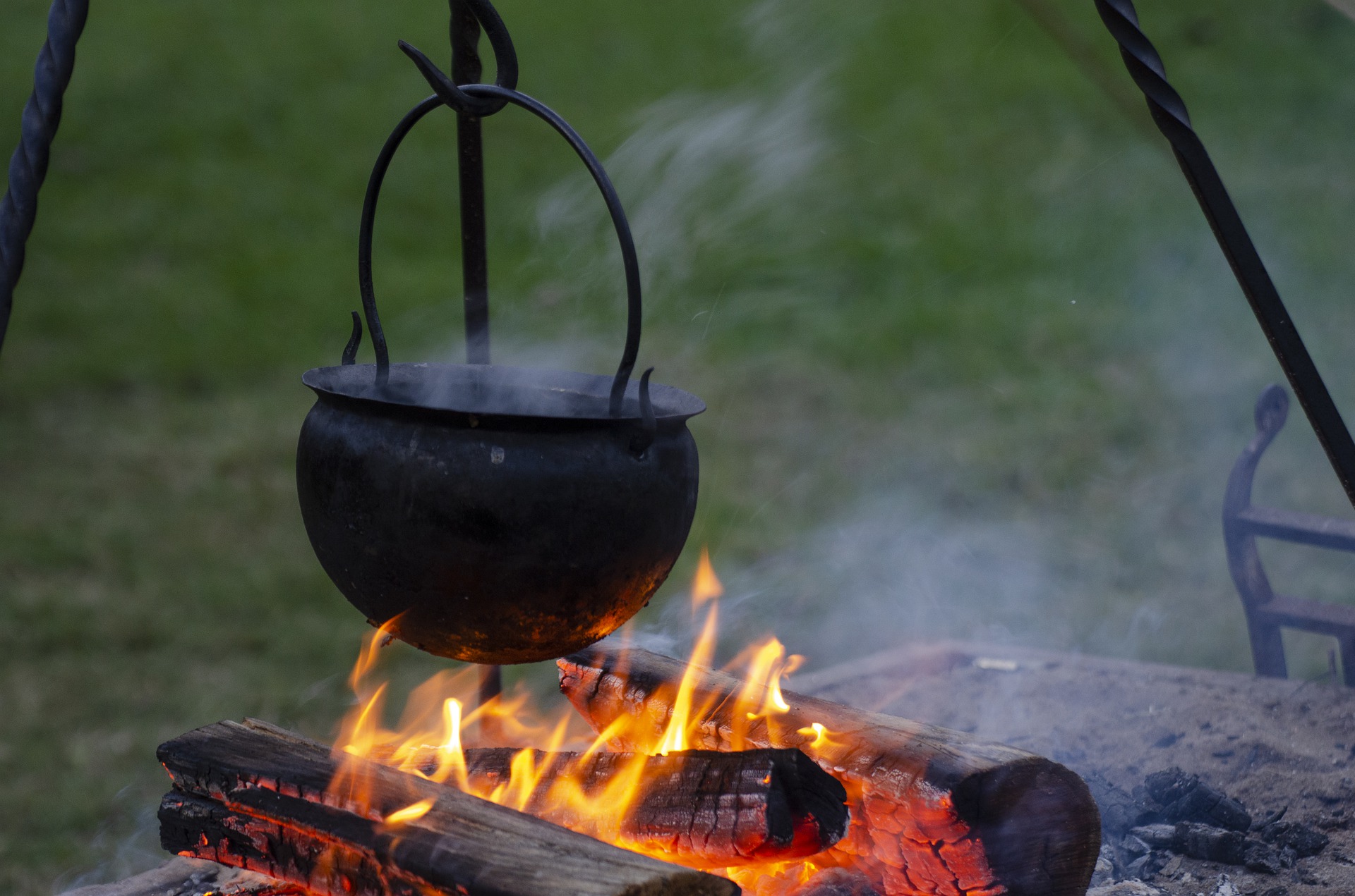 A cast iron cauldron hanging over a campfire.