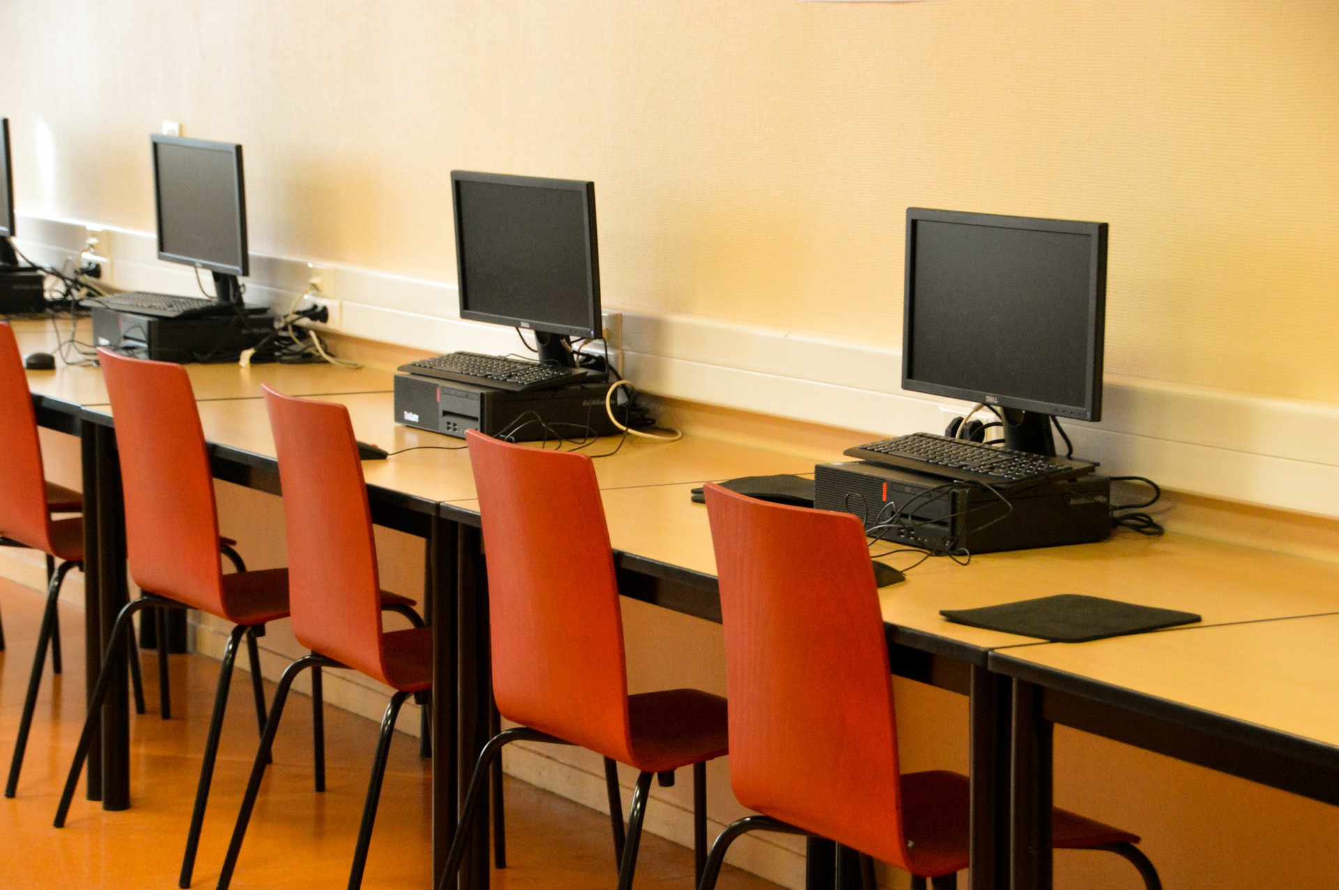 A row of computers with orange chairs in a classroom or computer lab.
