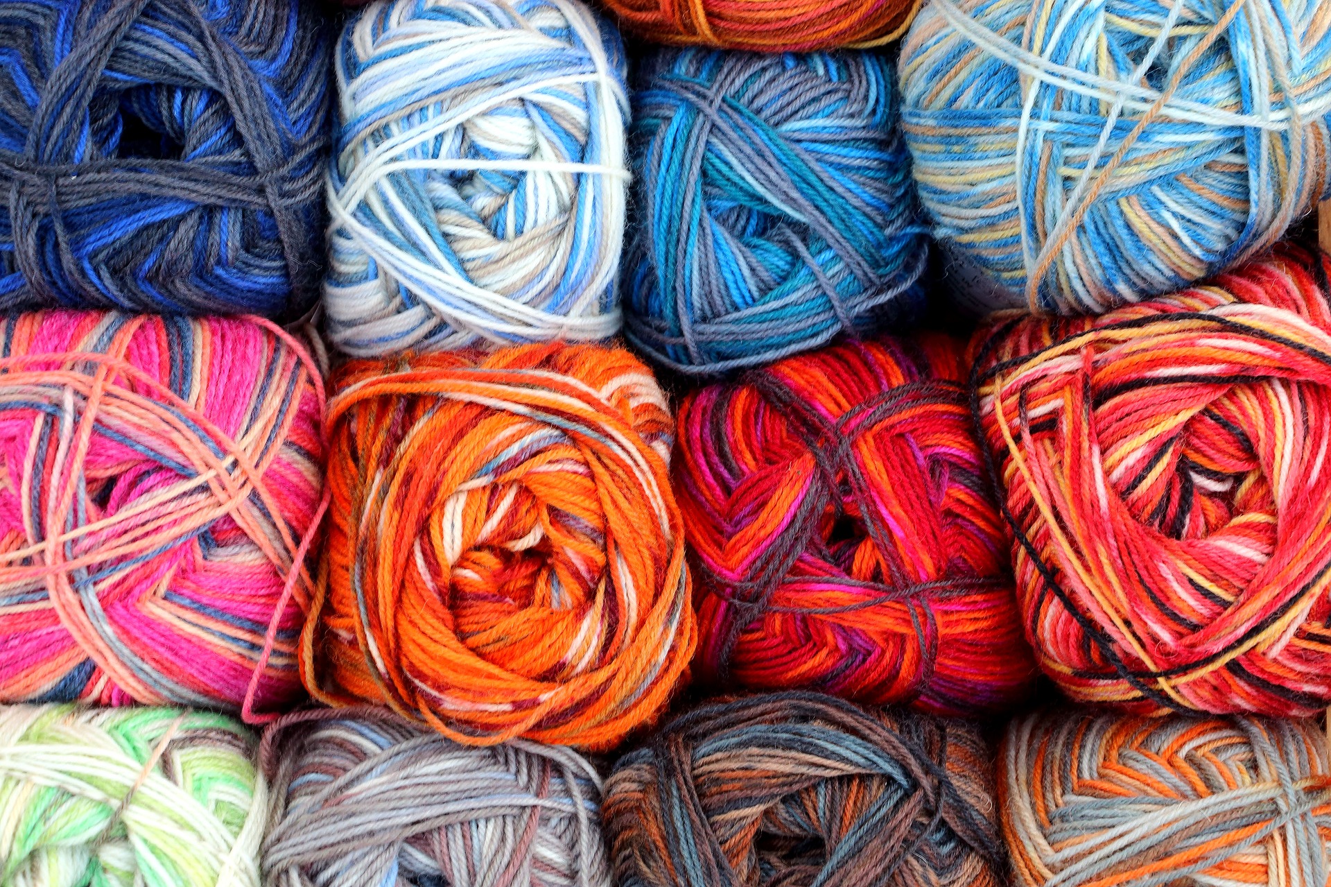 Twelve skeins of yarn are stacked 4 across. Each skein has a different variegated color pattern in shades of blues, reds, or greens.