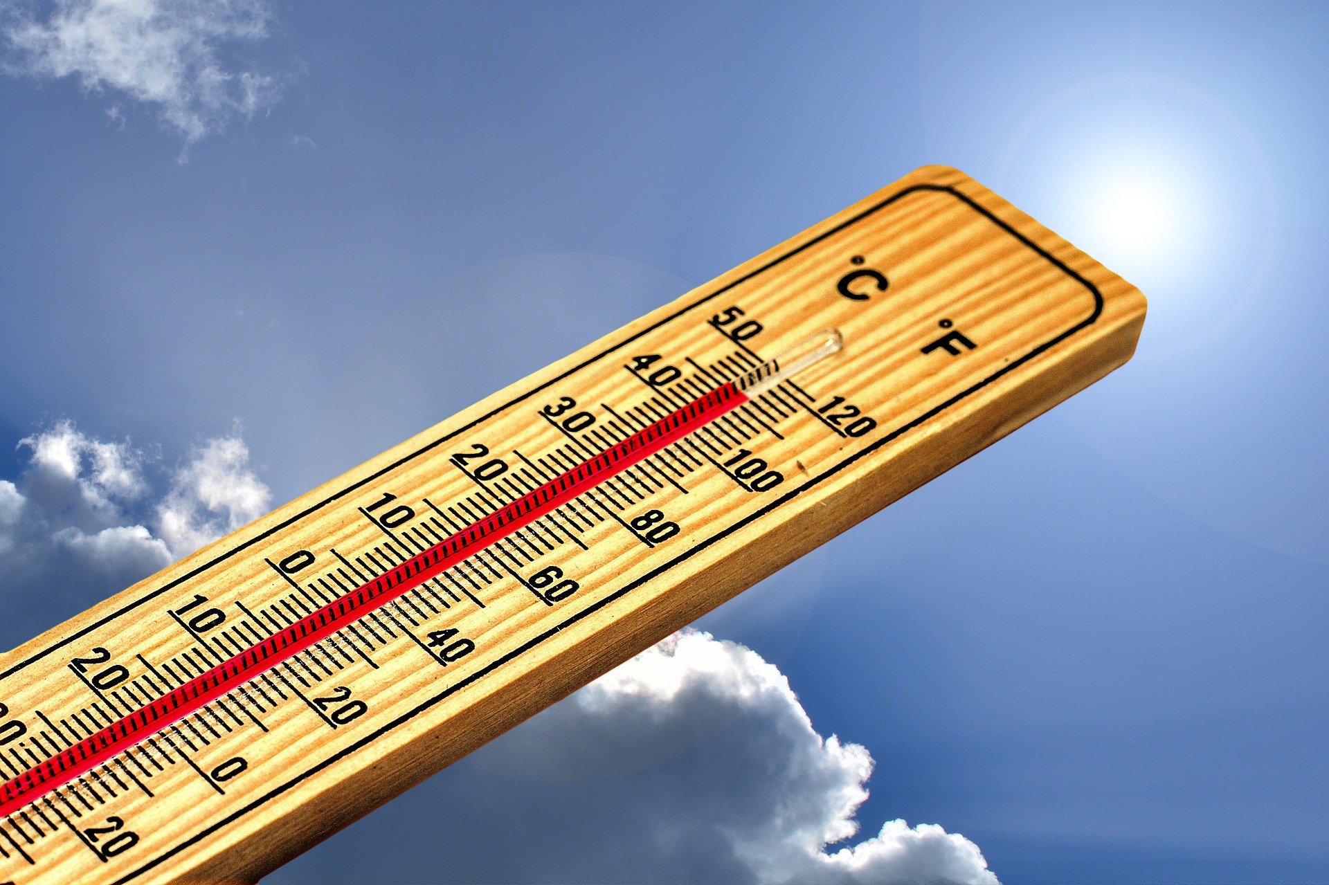 A wooden thermometer against a blue, partly cloudy sky reads 112 degrees Fahrenheit.
