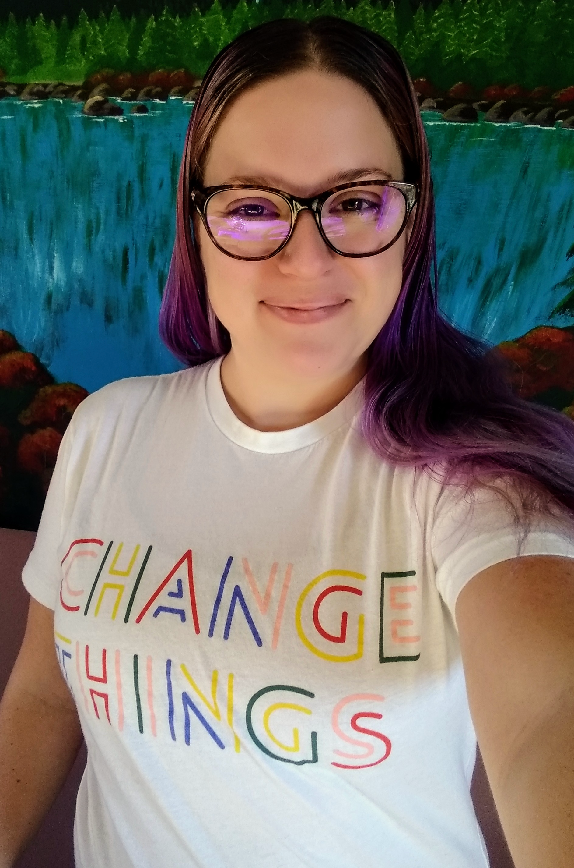 A selfie of Audrea Cook. She has long, purple hair and is wearing a white shirt that says "Change Things"